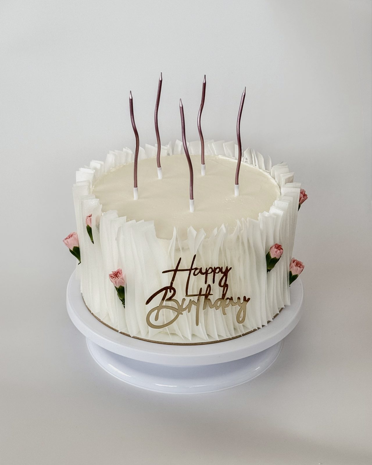 Bílý narozeninový dort s ruffle zdobením, růžovými karafiáty a nápisem Happy Birthday